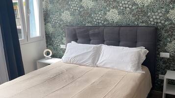 A neatly made bed with a beige cover, a dark headboard, and white pillows.