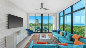 A modern living room with a large TV, a sofa set, a coffee table, and a view of the ocean. - Sunset Shores | Beachfront Condo w/ Premium Master, PVT Balcony & Upscale Decor (Melbourne Beach)