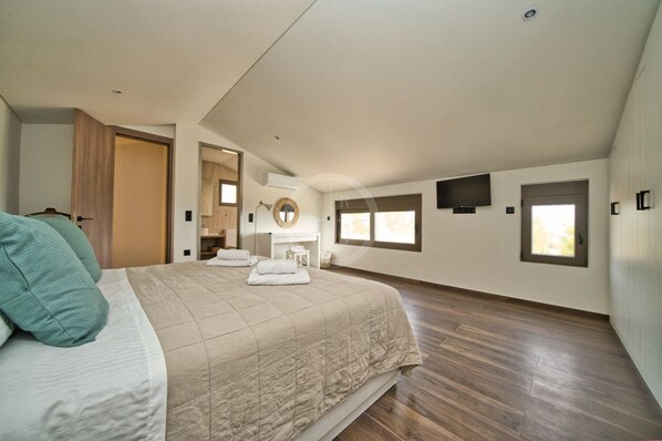 A spacious bedroom with a large bed, a walk-in closet, a vanity with a mirror, and a television mounted on the wall. - Evelinas View in Porto Heli (Porto Heli)