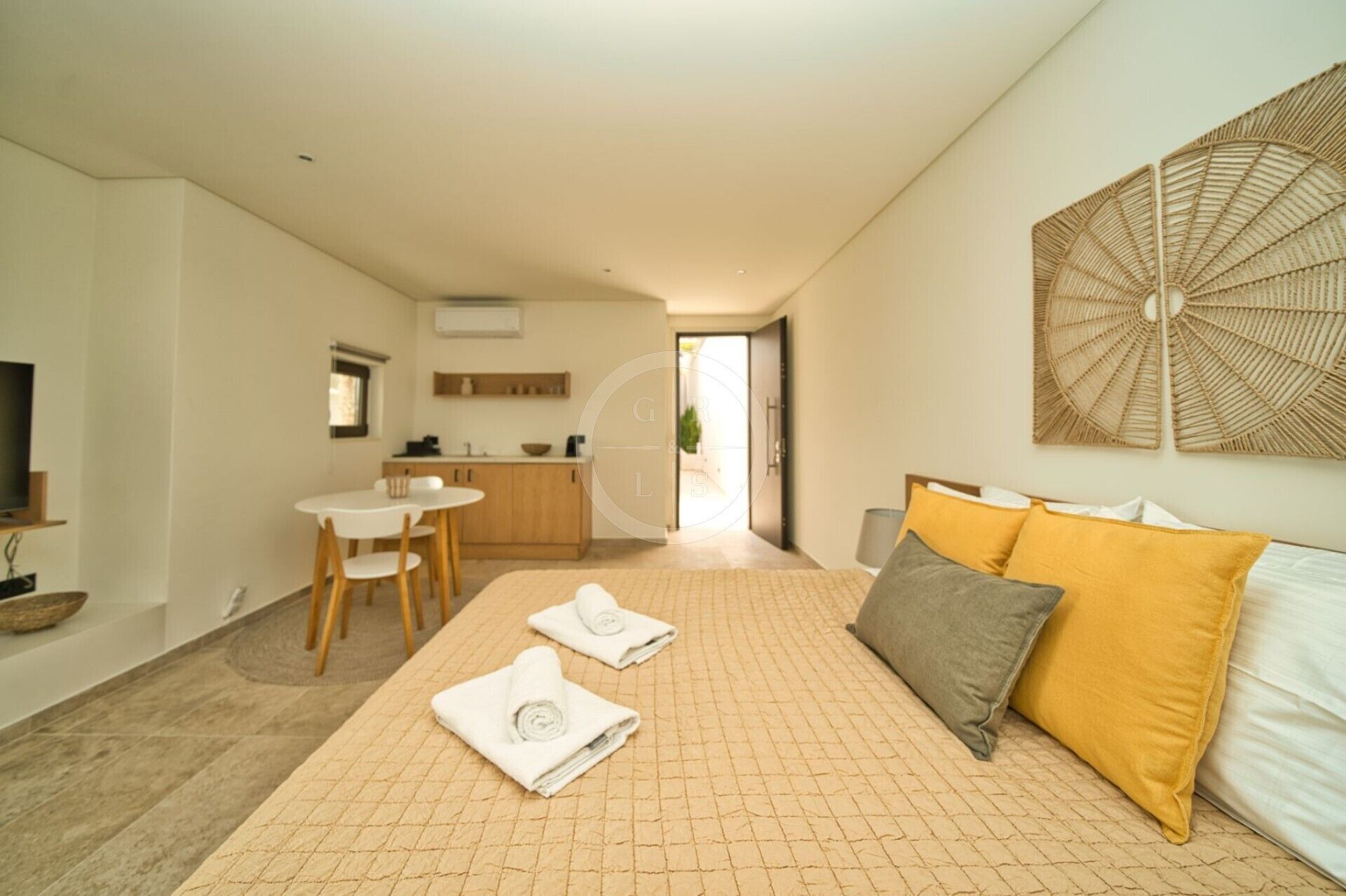 A modern hotel room with a large bed, a dining area, and a kitchen in the background.
