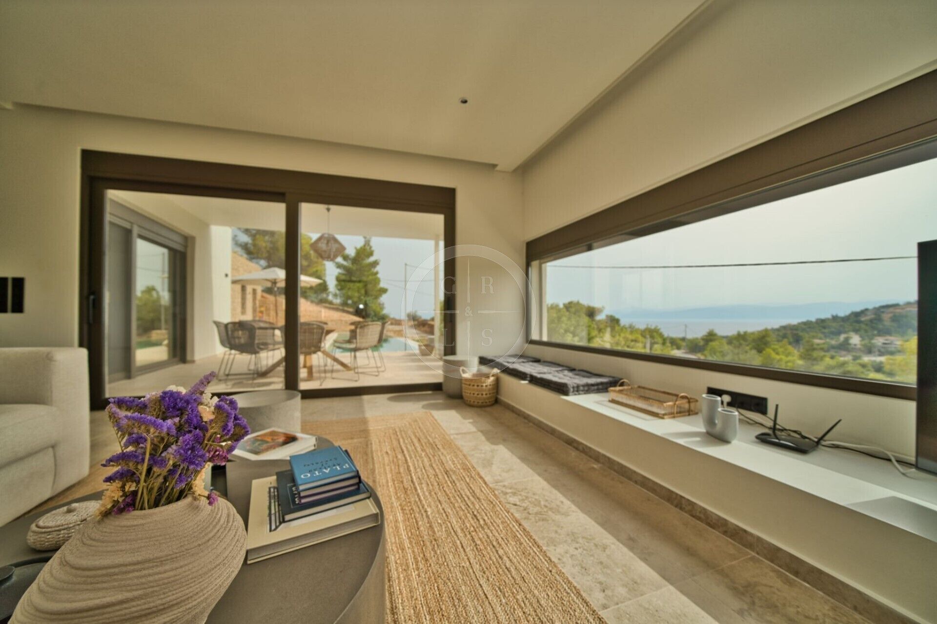 Ein modernes Wohnzimmer mit einem großen Fenster, das einen Blick auf einen Pool und Gartenmöbel bietet.