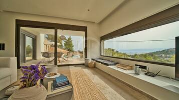 Ein modernes Wohnzimmer mit einem großen Fenster, das einen Blick auf einen Pool und Gartenmöbel bietet.