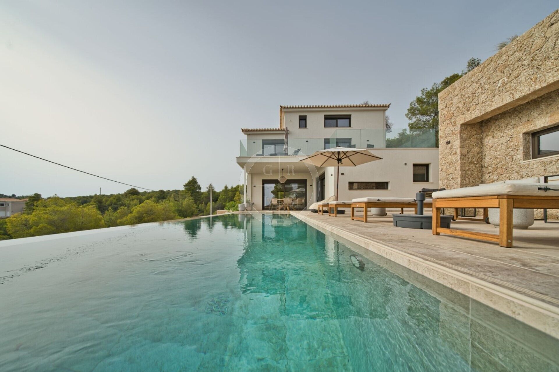 Eine moderne Villa mit privatem Infinity-Pool, Sitzgelegenheiten im Freien und einer Stein-Fassade.