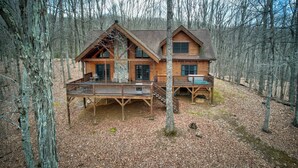 A log cabin with a deck and a porch, surrounded by a forest. - The Retreat (Banner Elk)