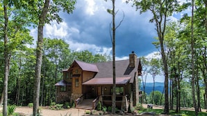 Une cabane rustique avec une cheminée en pierre, un revêtement extérieur en bois et une véranda avec des marches menant à une terrasse.