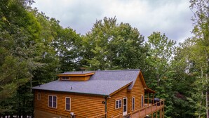 A log cabin with a balcony and a covered porch, surrounded by dense forest. - The Mountainbrier (Banner Elk)