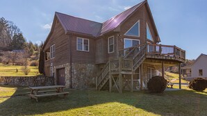 A wooden house with a stone foundation, a covered porch, and a picnic table. - River House at Meadow Landing (Fleetwood)