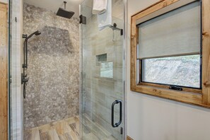 Eine Dusche mit Steinwand, Glastür und Fenster mit Holzrahmen.