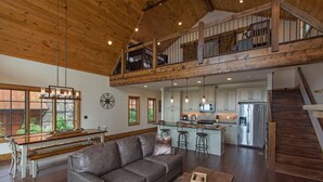 A spacious living area with a large gray sofa, a wooden coffee table, and a kitchen in the background. - Peregrine's Perch at Eagles Nest (Elk Park)