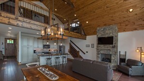 A spacious loft-style living area with a kitchen, wooden ceiling, stone fireplace, and a mezzanine level. - Peregrine's Perch at Eagles Nest (Elk Park)