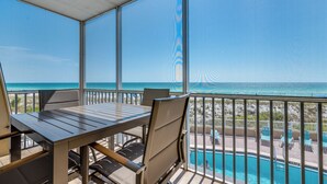A balcony with a table and chairs overlooking a pool and beach.