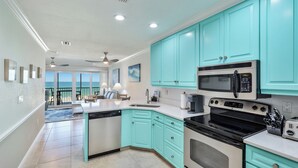 A kitchen with teal cabinets, a central island, a microwave, an oven, and a coffee maker.