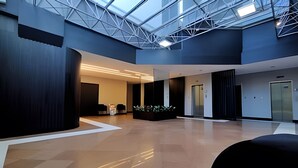 Un vestíbulo espacioso con techo alto, un atrio de cristal y una zona de recepción con decoración de plantas.