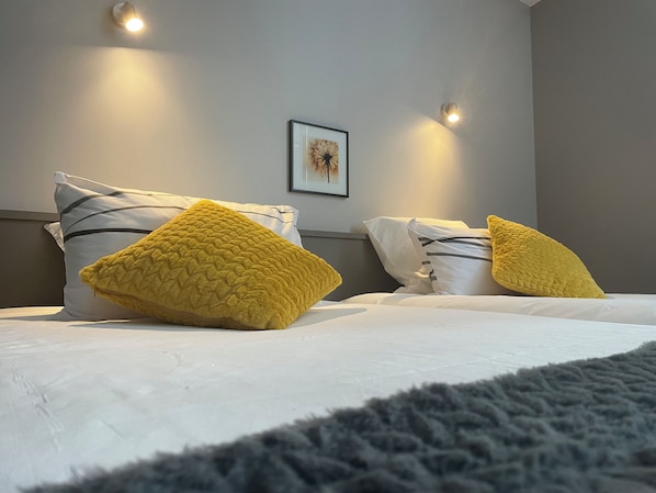 Habitación de hotel con cama, dos almohadas, un cuadro enmarcado en la pared y dos luces fijadas a la pared.