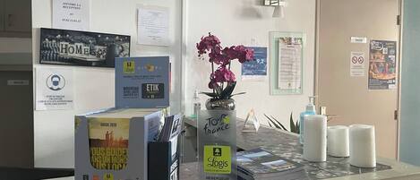 A hotel reception desk with a 'Home' sign, a 'Guide 2020' box, a 'For France' sign, and a 'Logis' brochure.