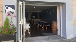 The entrance to Castel Restaurant with a sign above the door, a small outdoor seating area with a table and chairs, and a flower planter to the left. - Castel de Mirambel (Lourdes)