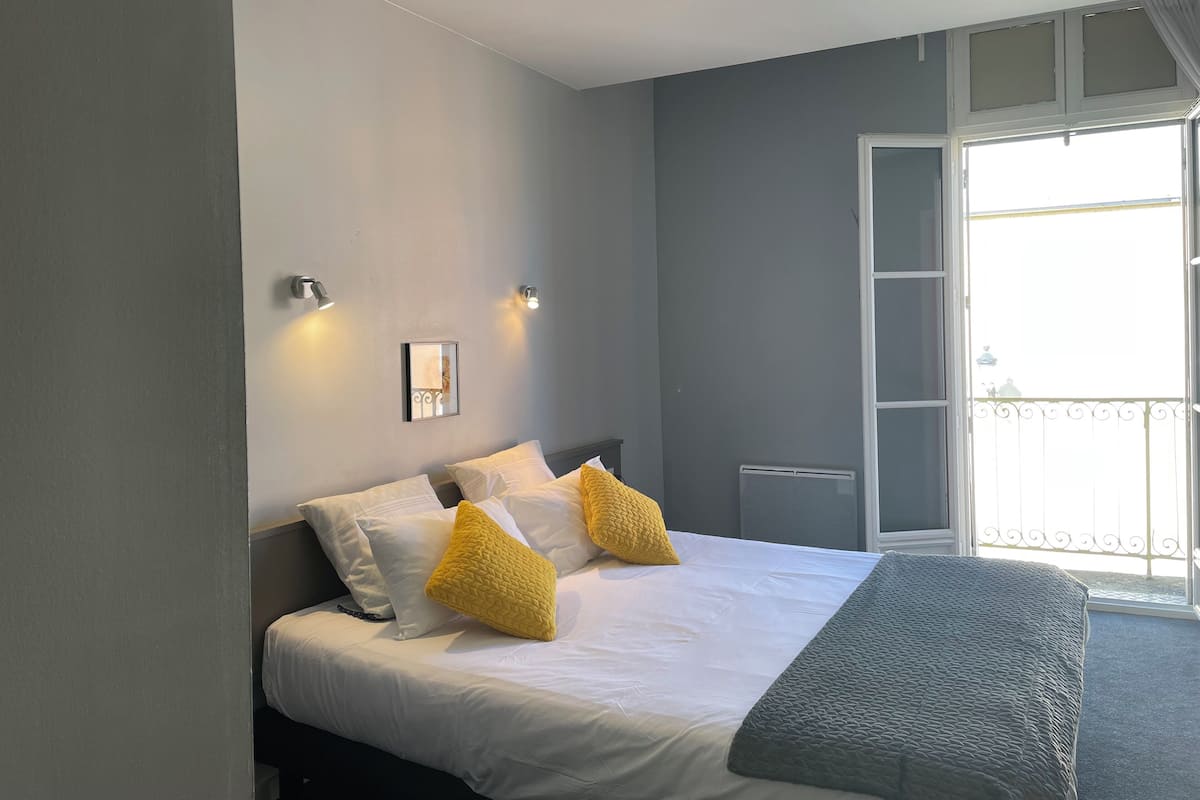 Un dormitorio con cama, dos lámparas de pared, una ventana con vistas y un radiador.