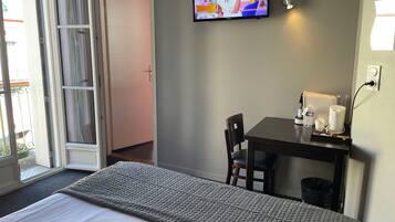 A hotel room with a bed, a TV on the wall, a small table with a chair, and a window with a view.