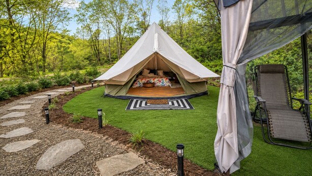 Une tente avec un lit à l’intérieur, entourée d’un jardin agrémenté d’un chemin de pierres et d’une chaise.