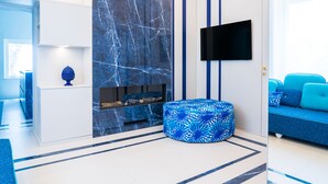 Ein modernes Wohnzimmer mit blauer und weißer Farbgestaltung, einem an der Wand befestigten Flachbildfernseher und einem blauen Sofa mit Kissen.