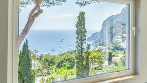 Ein Zimmer mit großem Fenster und Blick auf eine Küstenlandschaft mit Bäumen und Klippen.