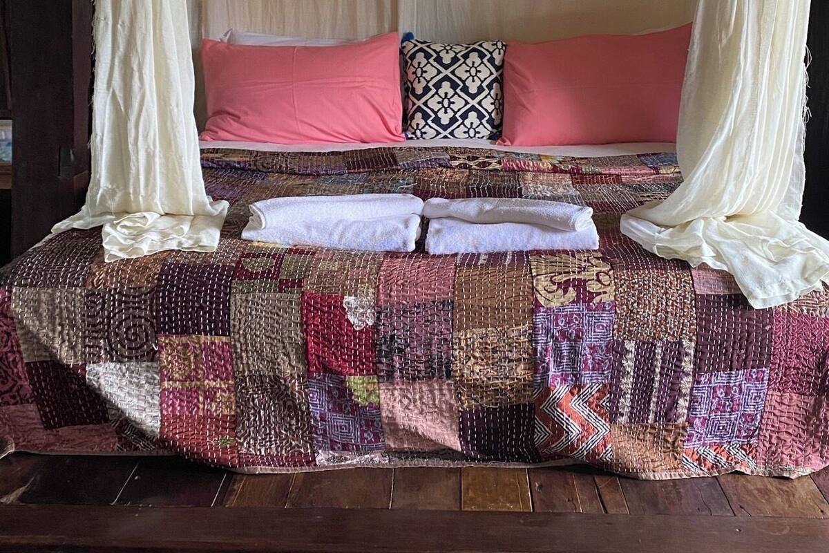 Una cama con dosel, varios almohadones y una colcha.