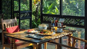 A dining table with breakfast items, a wicker basket, and a view of lush greenery through large windows. - Baan Mon Muan  (Mae Rim)