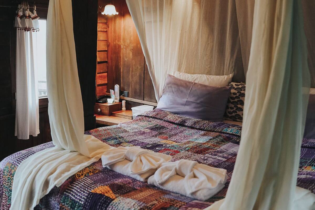 Una cama con dosel, una mesita de noche y una ventana con cortinas.