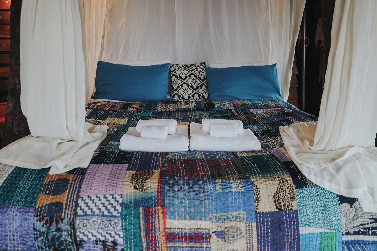 Una cama con colcha colorida, toallas blancas y almohadas azules.