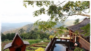 A wooden deck with a dining area, surrounded by lush greenery and a mountainous backdrop. - Baan Mon Muan  (Mae Rim)