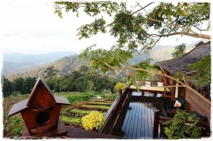 Una terraza de madera con zona de comedor, rodeada de exuberante vegetación y un paisaje montañoso.