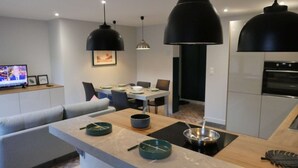 Ett modernt kök med en matplats, med en stor köksö utrustad med köksredskap, hängande lampor och en tv i bakgrunden.