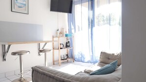 A modern living room with a sofa, a coffee table, a TV mounted on the wall, and a window with sheer curtains. - Oparadi "Le Nid" Avec sa Terrasse (Wimereux)