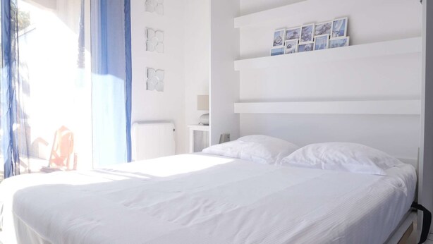 A bedroom with a large bed, a nightstand, a wall-mounted shelf with pictures, and a window with curtains. - Oparadi "Le Nid" Avec sa Terrasse (Wimereux)
