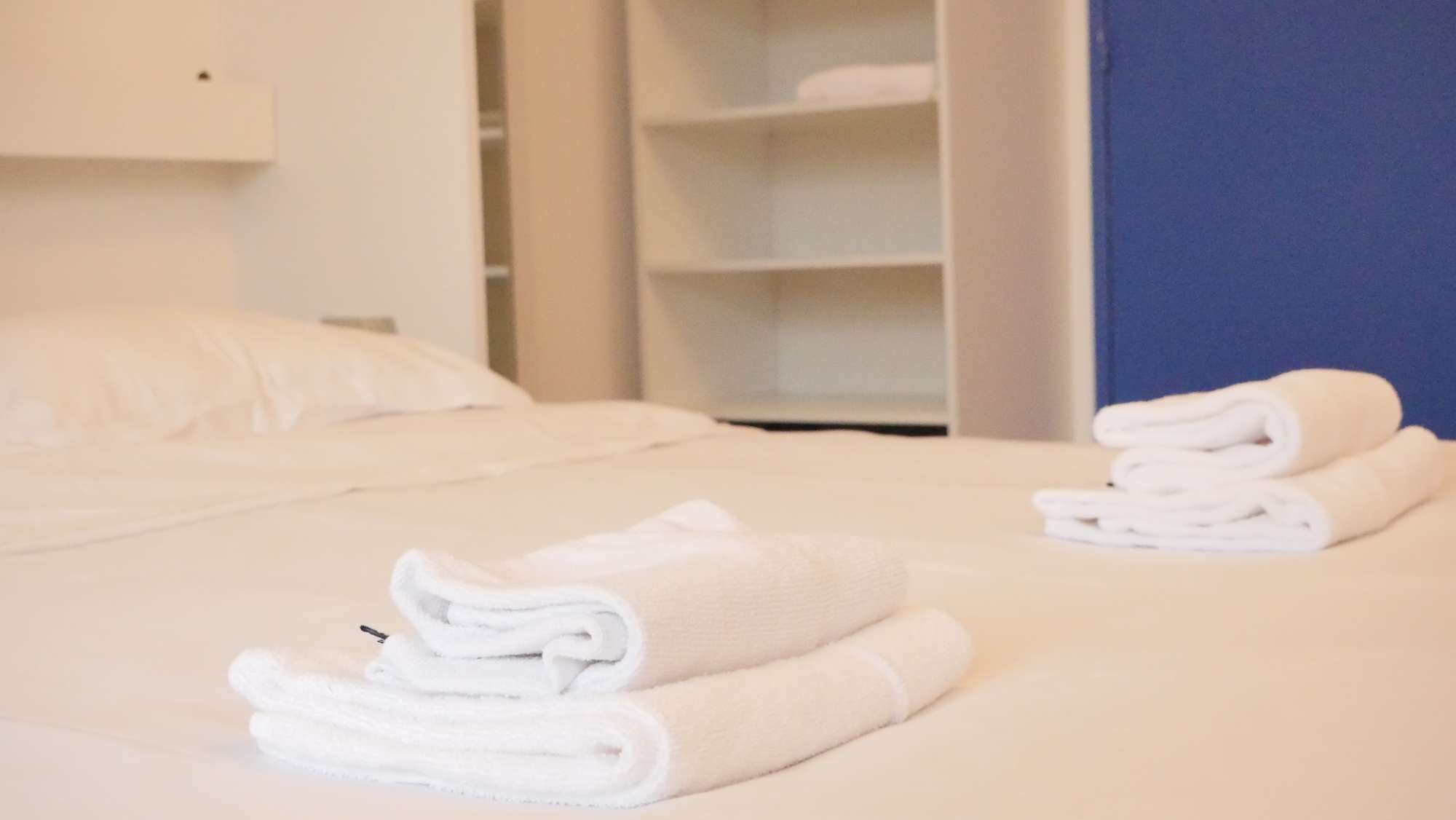 A neatly made bed with folded white towels and a closed wardrobe in a hotel room.