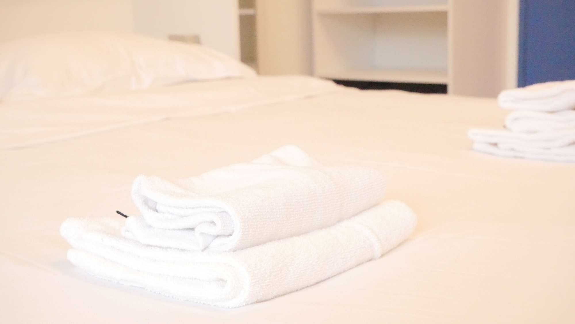 A neatly made bed with folded white towels and a white pillow.