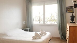 Een hotelkamer met een bed, een raam met gordijnen, een klein tafeltje en een houten dressoir.