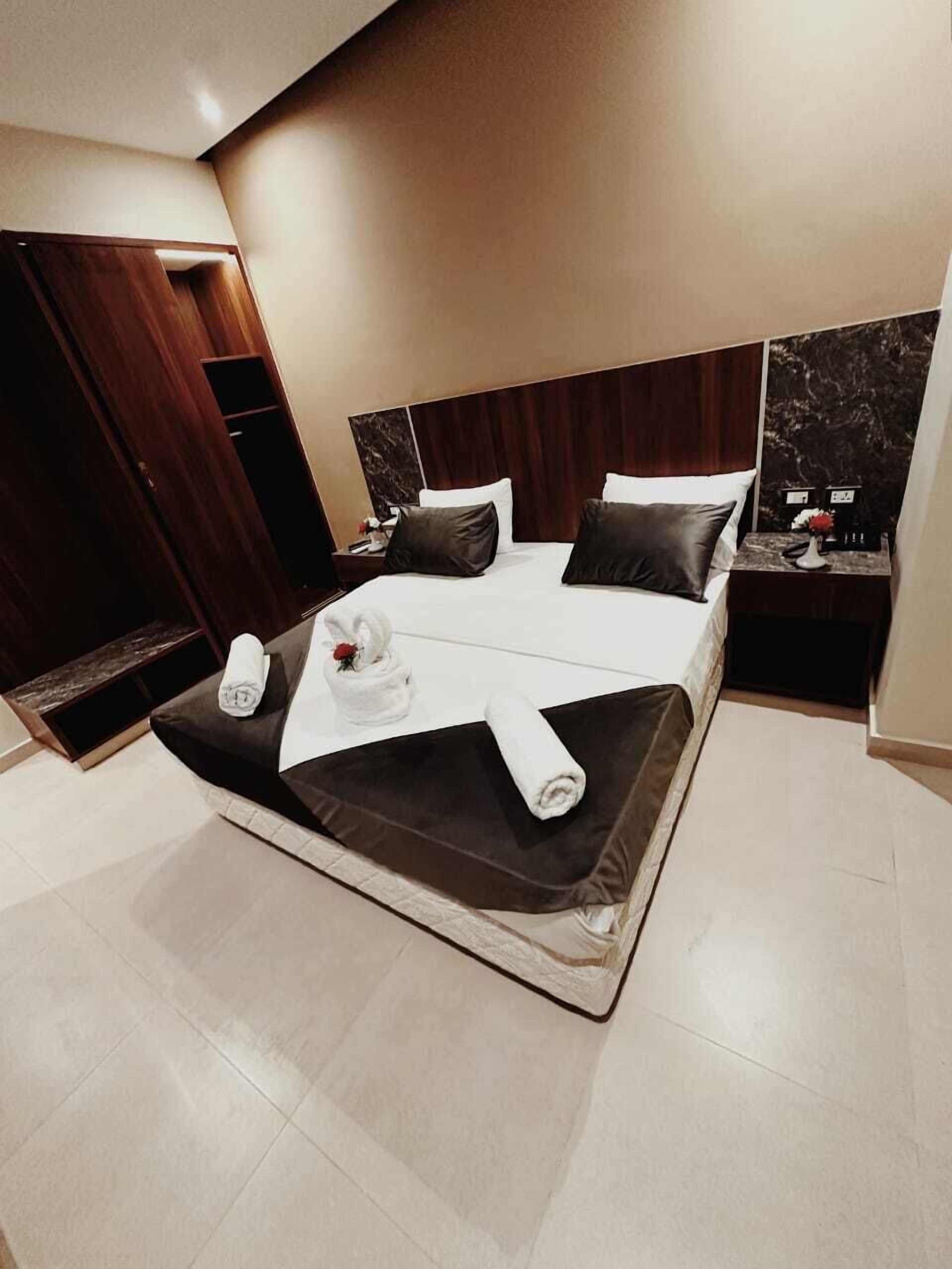 A modern hotel room with a large bed, dark wood headboard, and a marble accent wall.