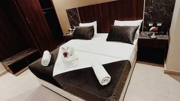 A modern hotel room with a large bed, dark wood headboard, and a marble accent wall.