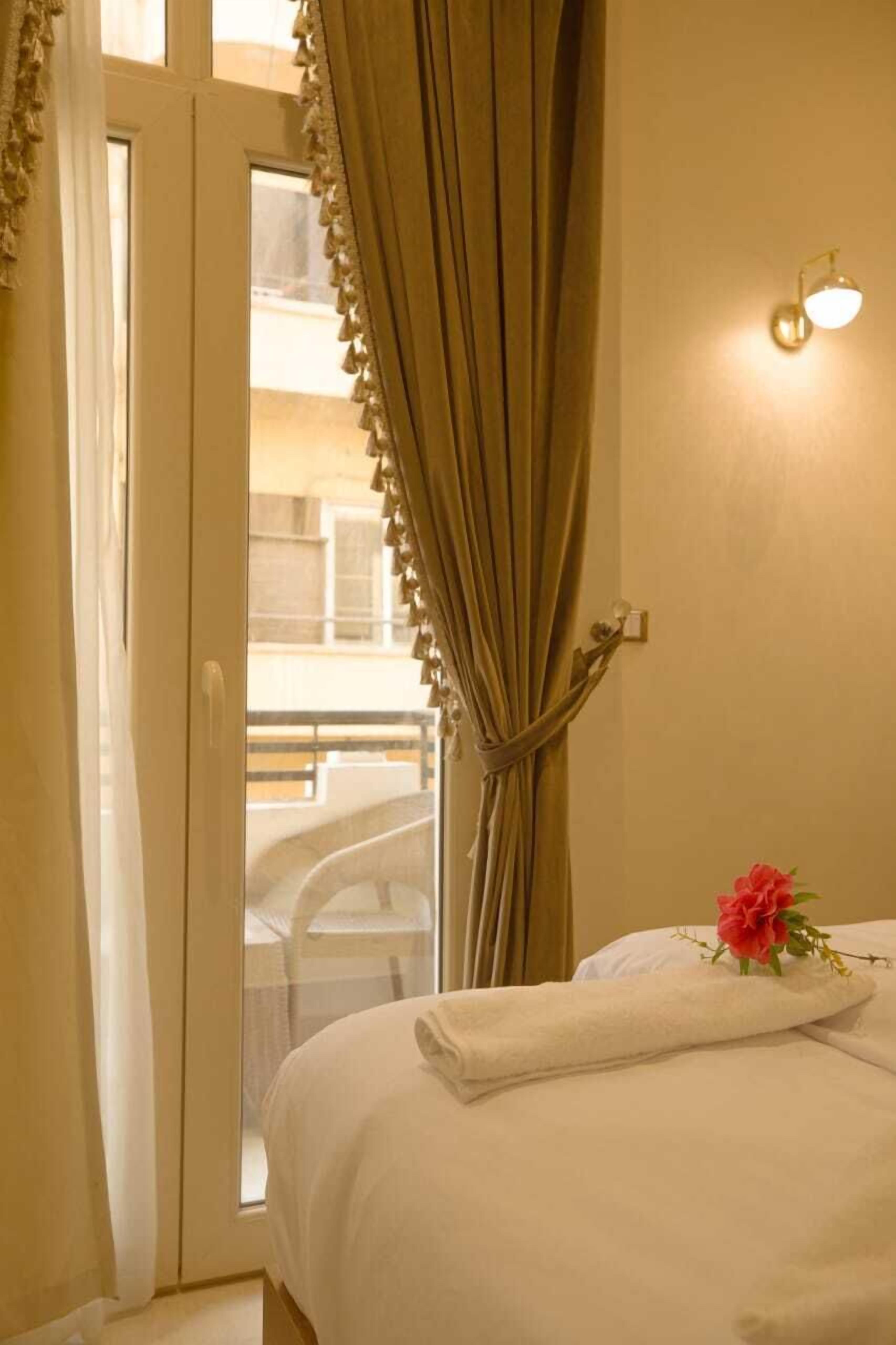 A hotel room with a bed, a window with curtains, a balcony, and a wall-mounted light.
