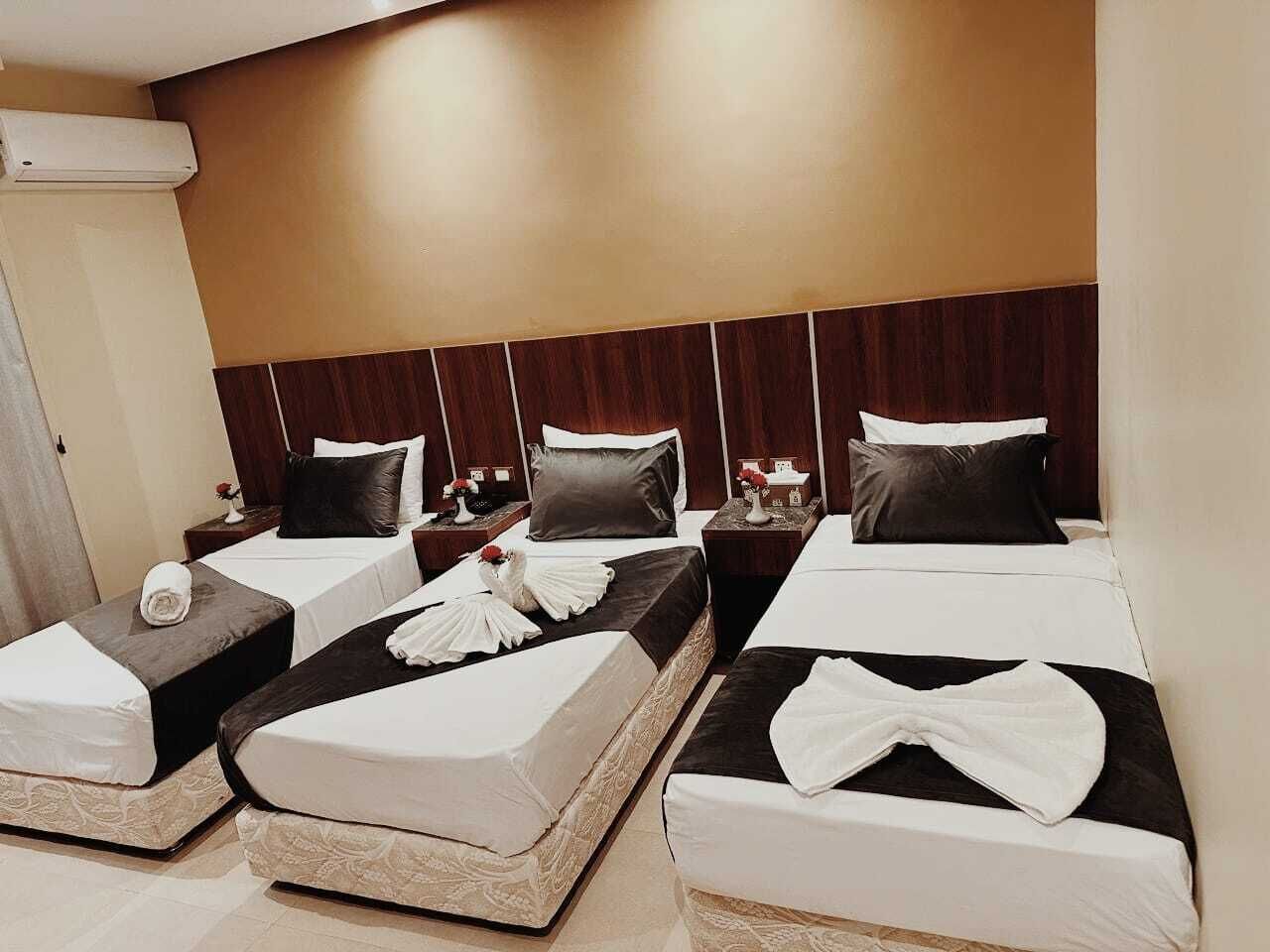 Une chambre d’hôtel avec trois lits, chacun recouvert d’une courtepointe blanche et doté d’une tête de lit noire. Chaque lit est agrémenté d’une serviette blanche et d’un objet décoratif blanc.
