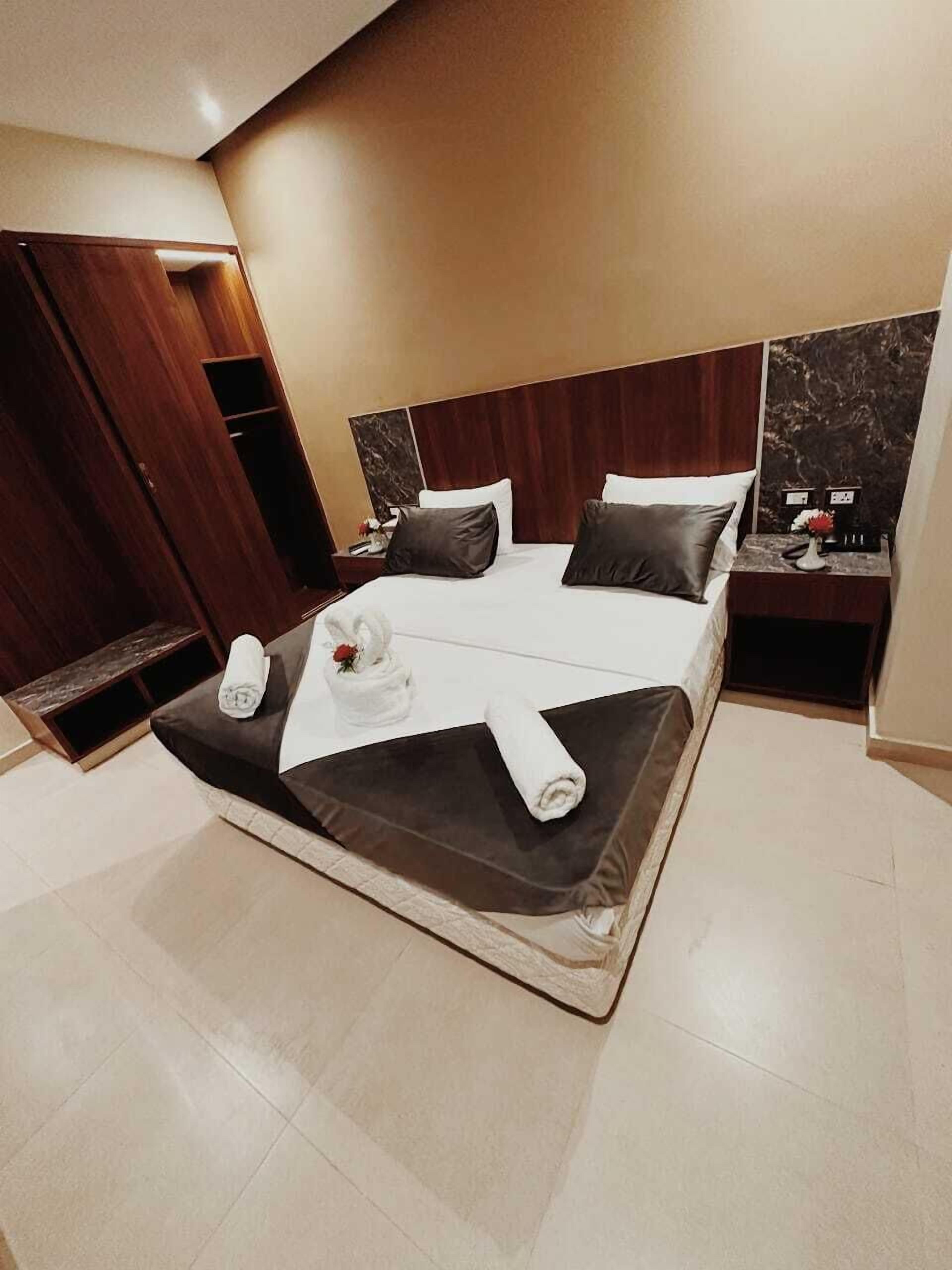 A modern hotel room with a large bed, wooden headboard, and a marble accent wall.