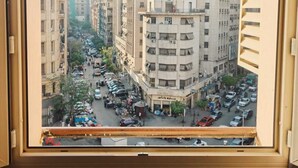 A view through a window of a city street with buildings, vehicles, and pedestrians. - Sama hotel (Cairo)