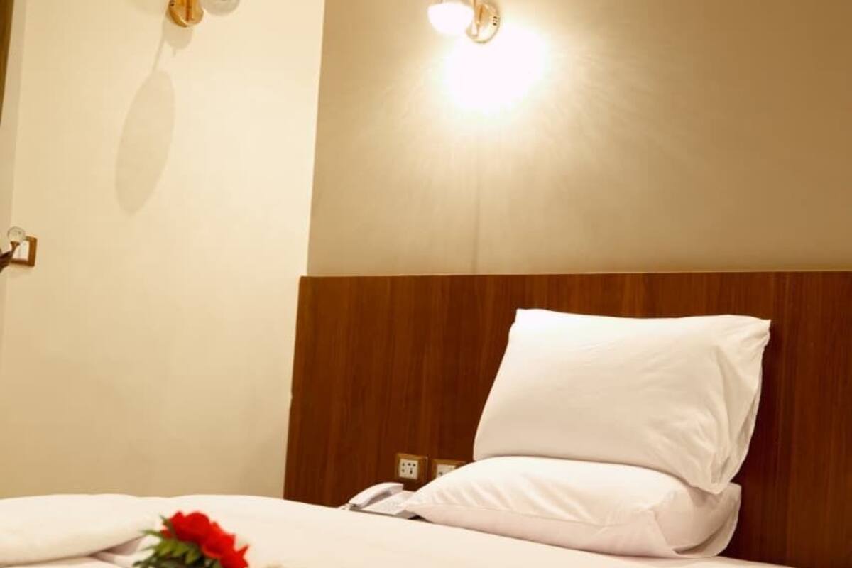A hotel room with a bed, white linens, a wooden headboard, and two wall-mounted light fixtures.