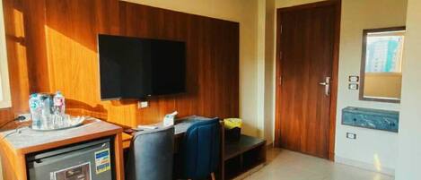 A hotel room with a desk, chair, television, minibar, and a door leading to another room.