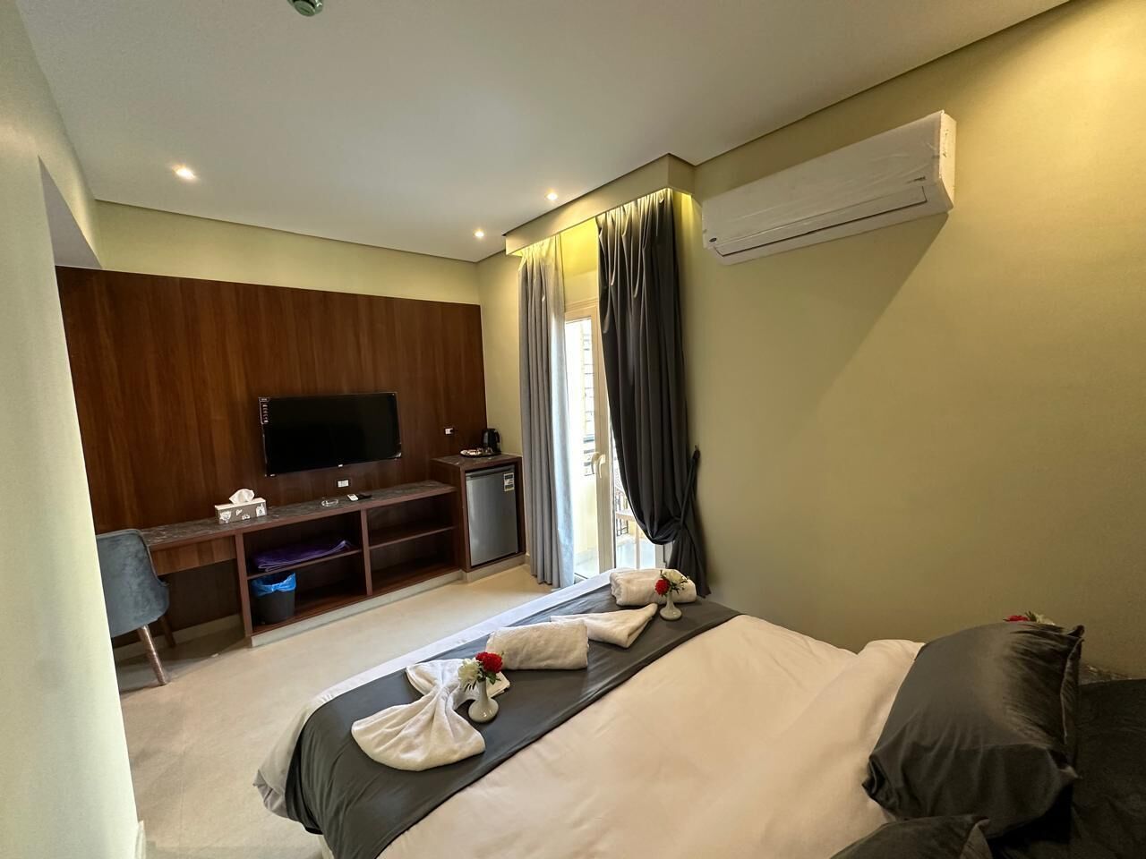 Ein Hotelzimmer mit einem Bett, einem Schreibtisch mit Fernseher, einer kleinen Kühlbox und einem Fenster mit Vorhängen.