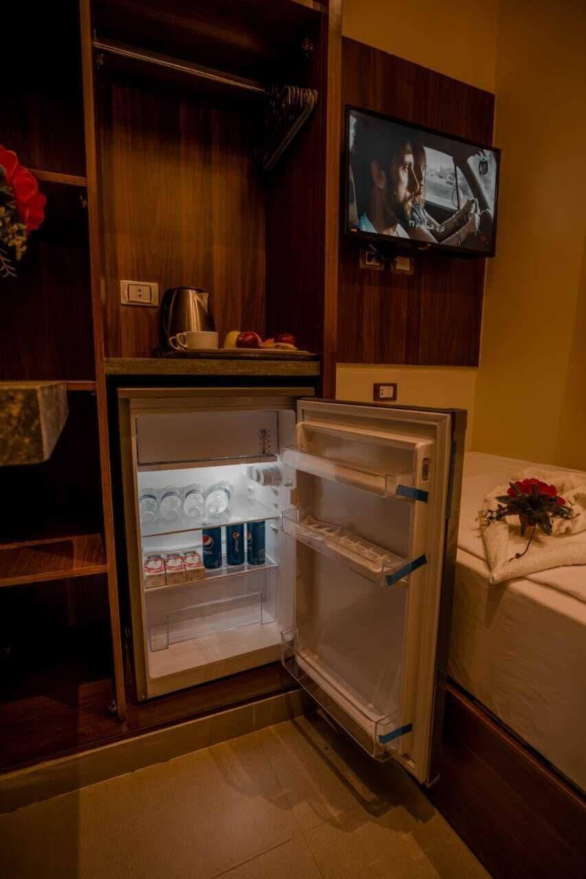 Una stanza compatta con frigorifero integrato, televisione a muro e un tavolino con bollitore e tazze.