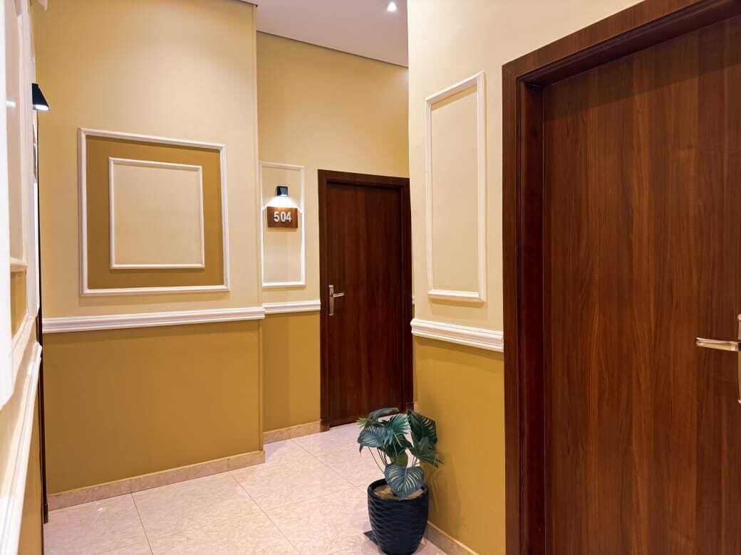 A hallway with a potted plant, a door with a number sign, and a light fixture.
