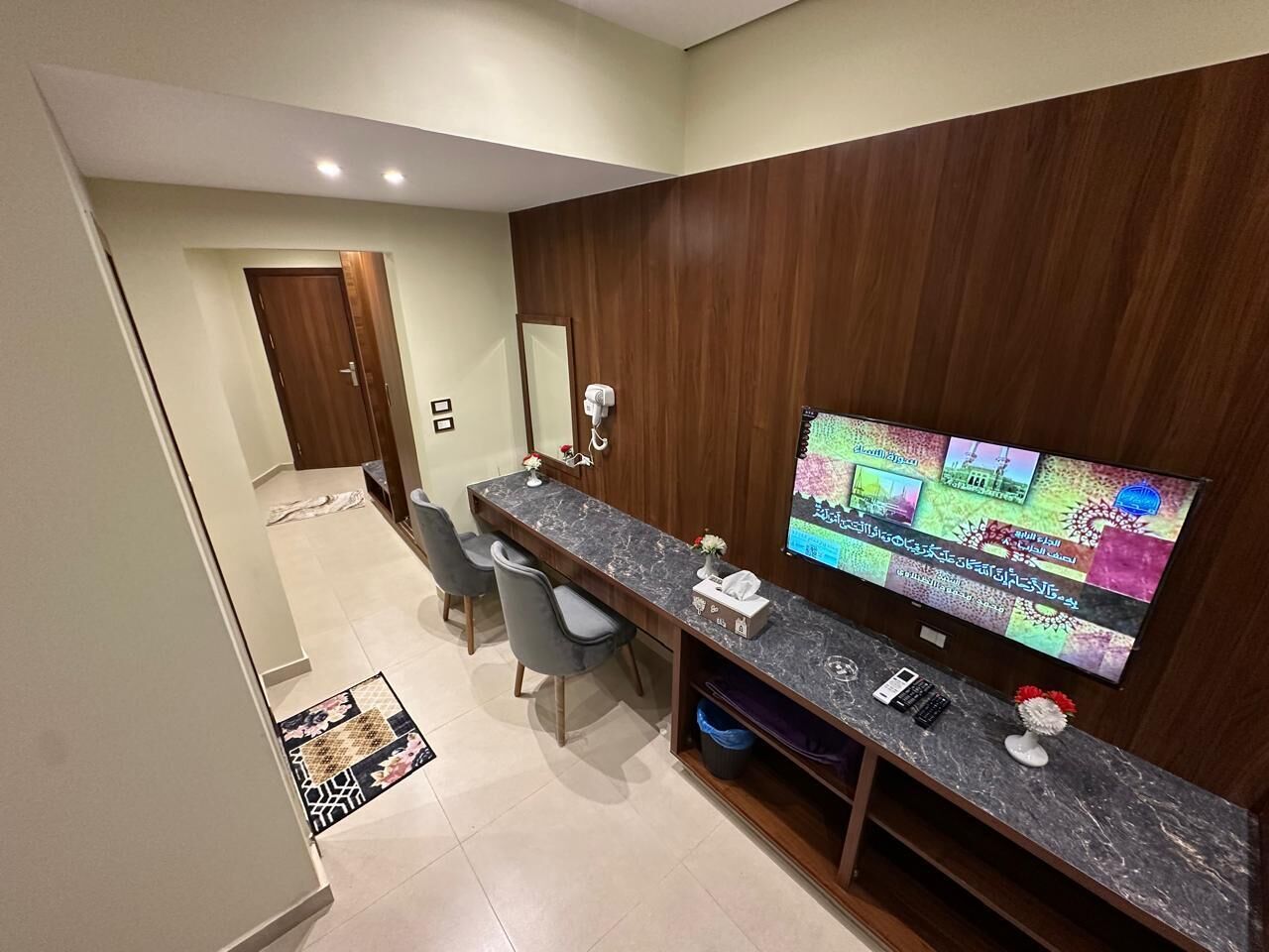 A modern kitchen with a marble countertop, a built-in oven, and a large flat-screen TV mounted on the wall.