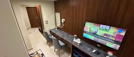 A modern kitchen with a marble countertop, a built-in oven, and a large flat-screen TV mounted on the wall.